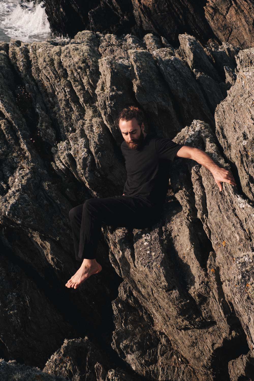 Man climbing down a rock face wearing So We Flow...