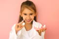 Photo of a little girl smiling holding a teeth model in front of pink background