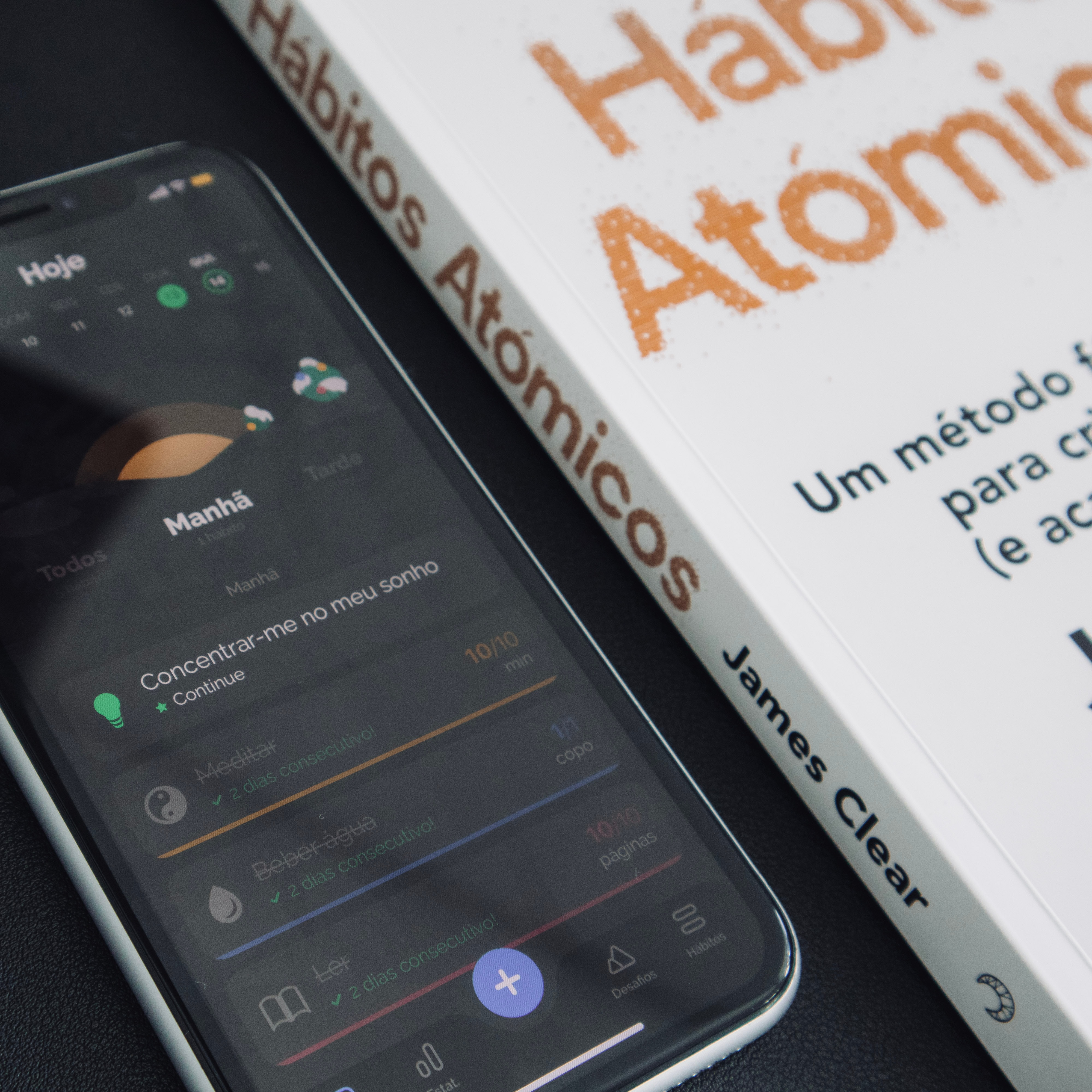 Atomic habits book next to a habit tracker mobile app