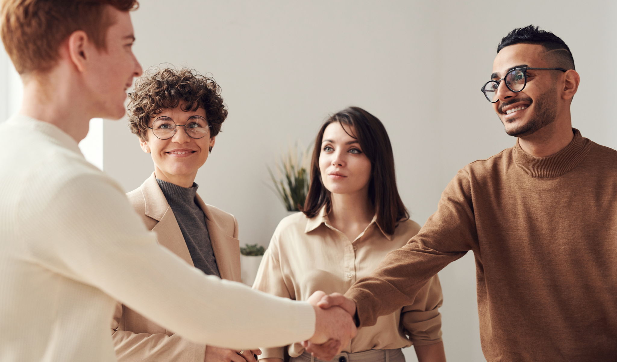 A group of young professionals sharply dressed and attractive, shaking hands and smiling.