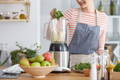 woman wearing an apron, adding greens to her blender and making a smoothie