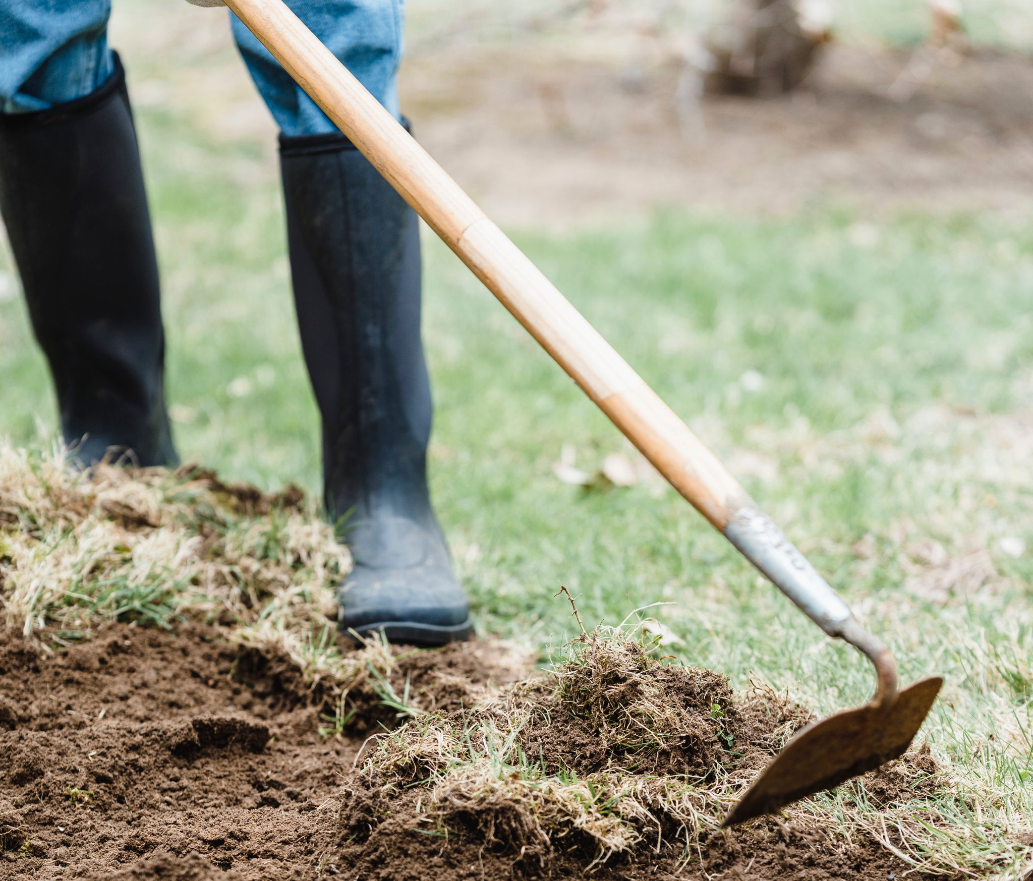 A person using a hoe wearing garden boots