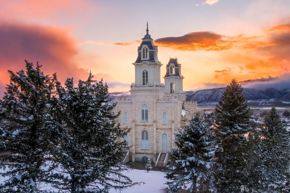 Manti Temple standing against an orange sky and surrounded by snowy trees. 