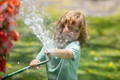 Child enjoying summer themed sensory play by spraying water from a garden hose outdoors.