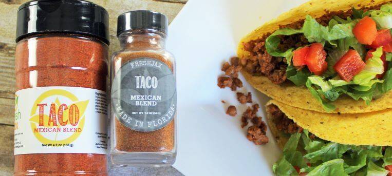 FreshJax Organic Taco Seasoning next to a plate of two hard shell tacos filled with chickpeas, tomatoes, and lettuce.