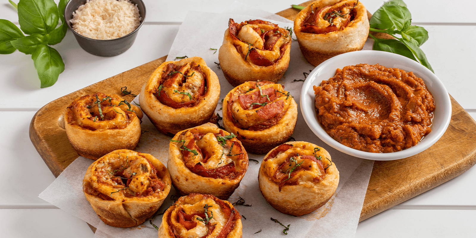 ZENB Pepperoni Pizza Rolls served with a small bowl of marinara sauce atop a wooden serving platter on a white table.