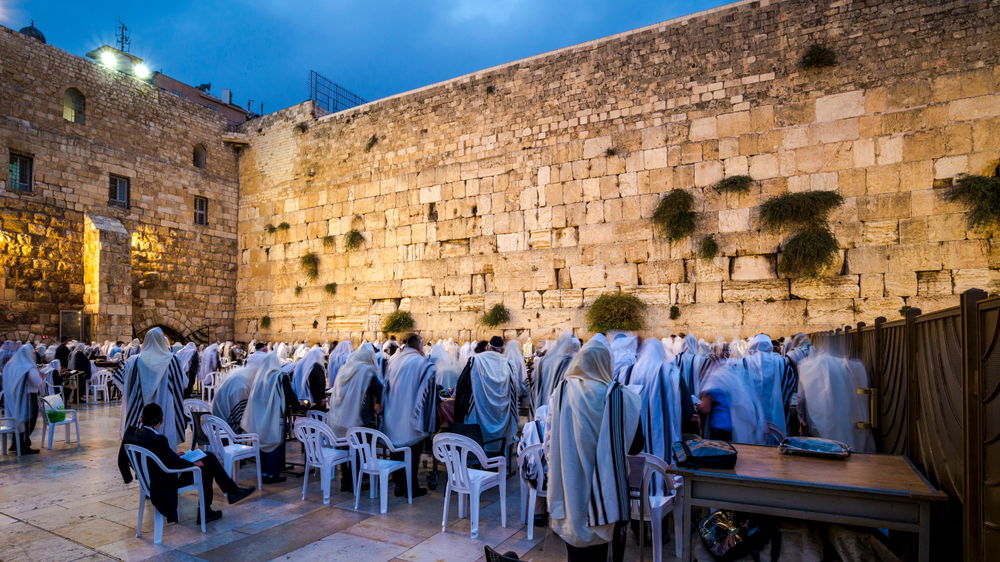 Orthodox Jewish men in Tallit prayer shawls standing from before dawn for Shacharit sunrise prayer at the WesternWailing Wall or Kotel, the holiest place in Judaism; Jerusalem Israel