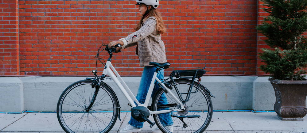 a woman walking next to a white electric city bike in front of a red brick wall