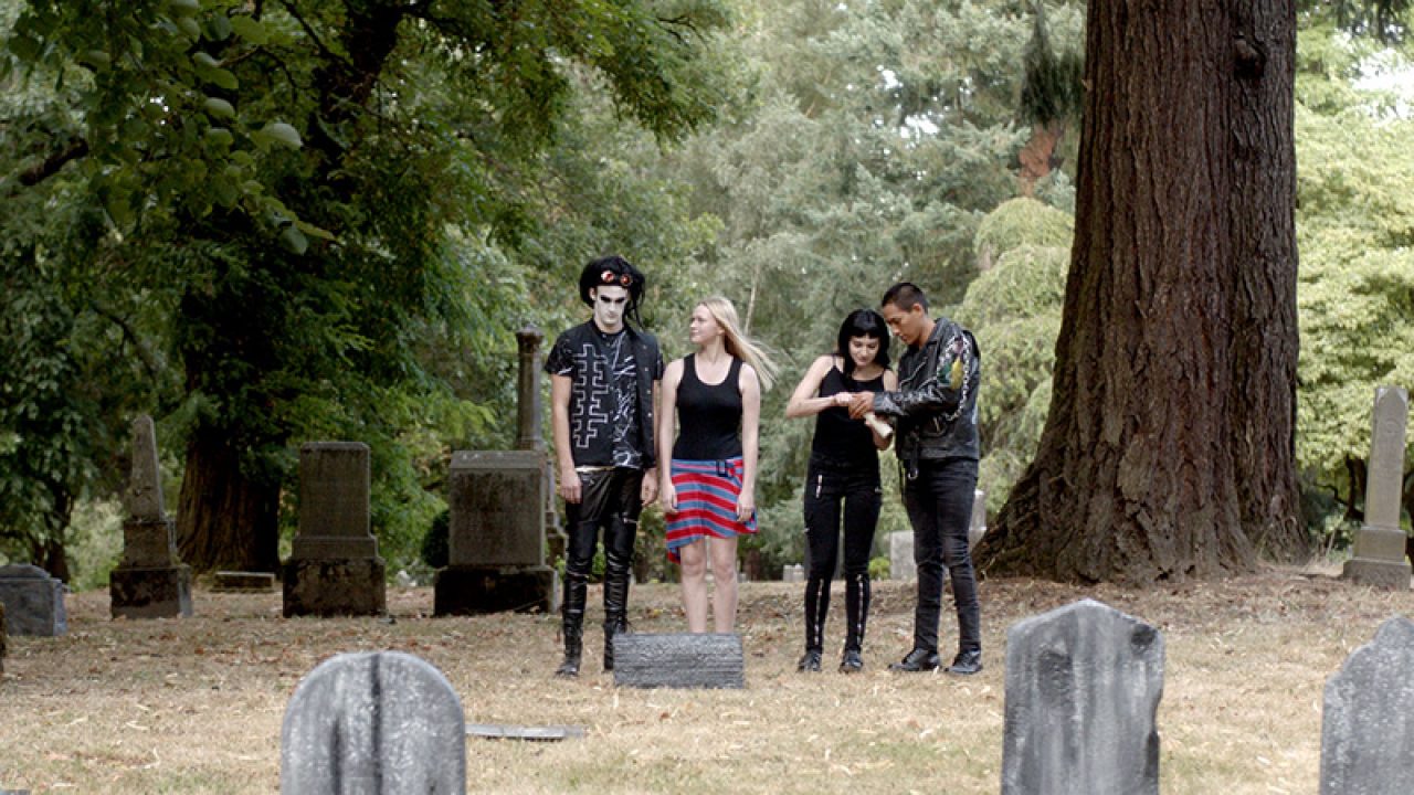 The 4 friends from the film standing in front of a gravestone at a cementary.