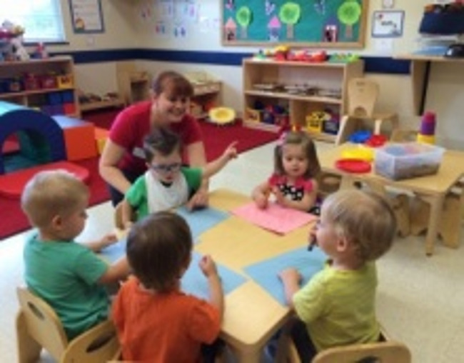 Primrose toddler students sit with drawing sheets and crayons in class as their teacher interacts with them