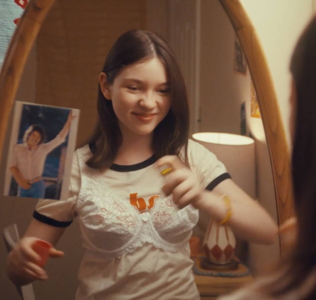 Young girl, smiling,  in front of mirror applying some Love's Baby Soft coologne on her. 