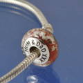 A memorial glass bead in red, containing mum and dads cremated ashes