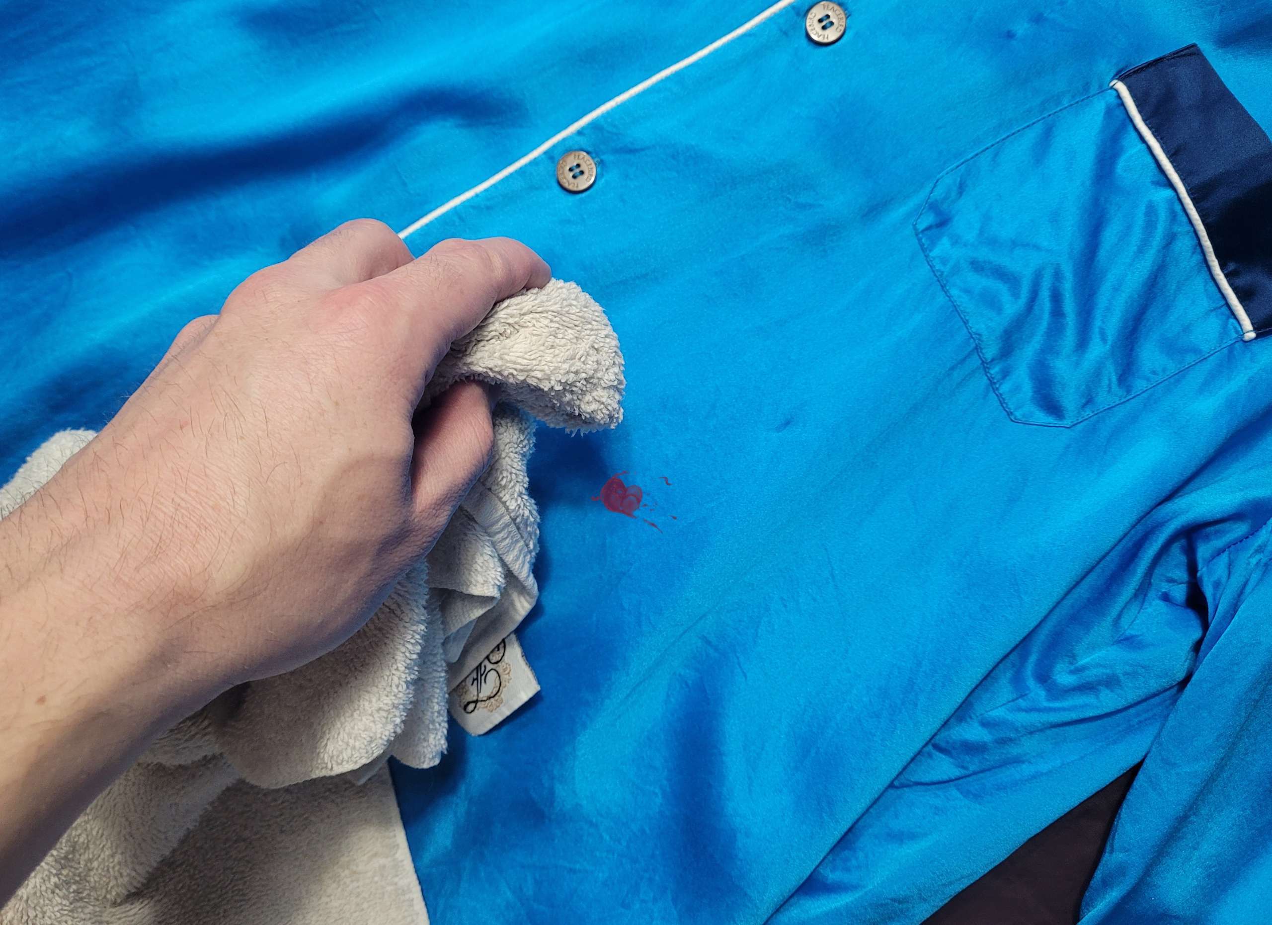 a photo showing a man using a cloth to dab a stain off of a blue silk shirt