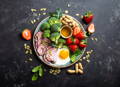 a colorful plate of food including ham, broccoli, nuts, strawberries, eggs, and spinach