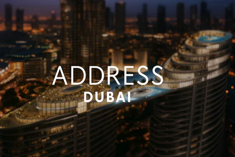 Luxurious Address Dubai hotel building at night, showing its unique architecture and stunning rooftop infinity pool with city lights in the background.