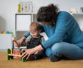 A mother and her toddler sitting on a playroom floor and playing with a colorful wooden Montessori hammering toy.