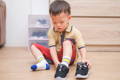 Little Asian boy sitting and concentrating on putting his shoes on. 