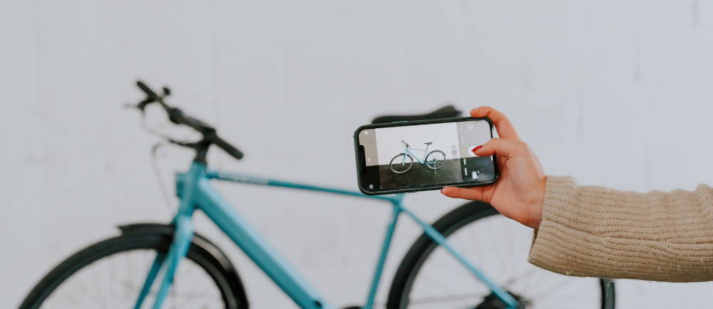 a woman using an iphone to take a photo of an electric city bike against a white backdrop
