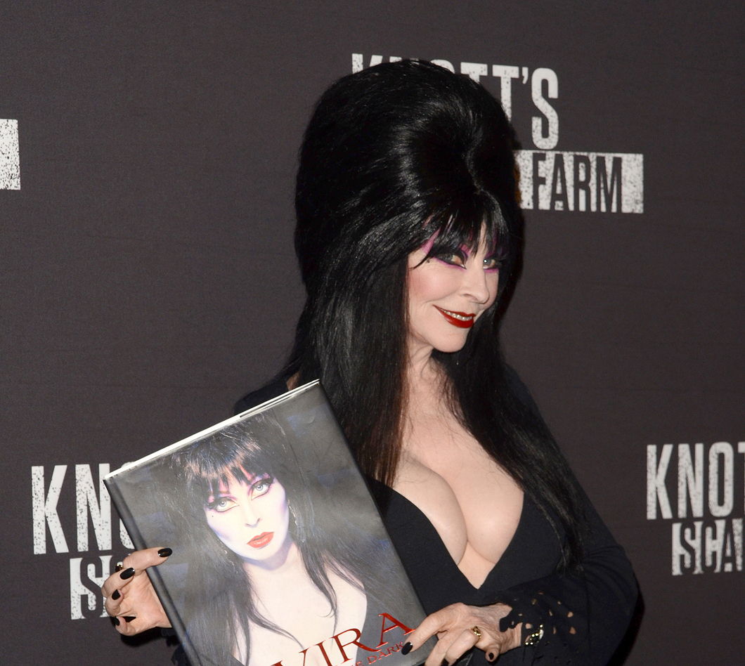 Elvira at the 2016 Knott's Scary Farm at Knott's Berry Farm holding her book and smiling.