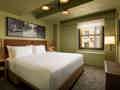 Ein modernes Hotelzimmer mit Kingsize-Bett, Stadtblick, Wandfernseher und zeitgenössischer Beleuchtung.