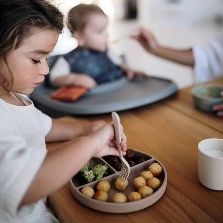 Little girl using a fork from the Montessori First Bites Gift Set to eat from her plate.