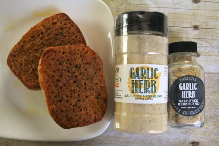 A plate with two slices of garlic and herb bread next to two bottles of FreshJax Organic Garlic and Herb spice blend.