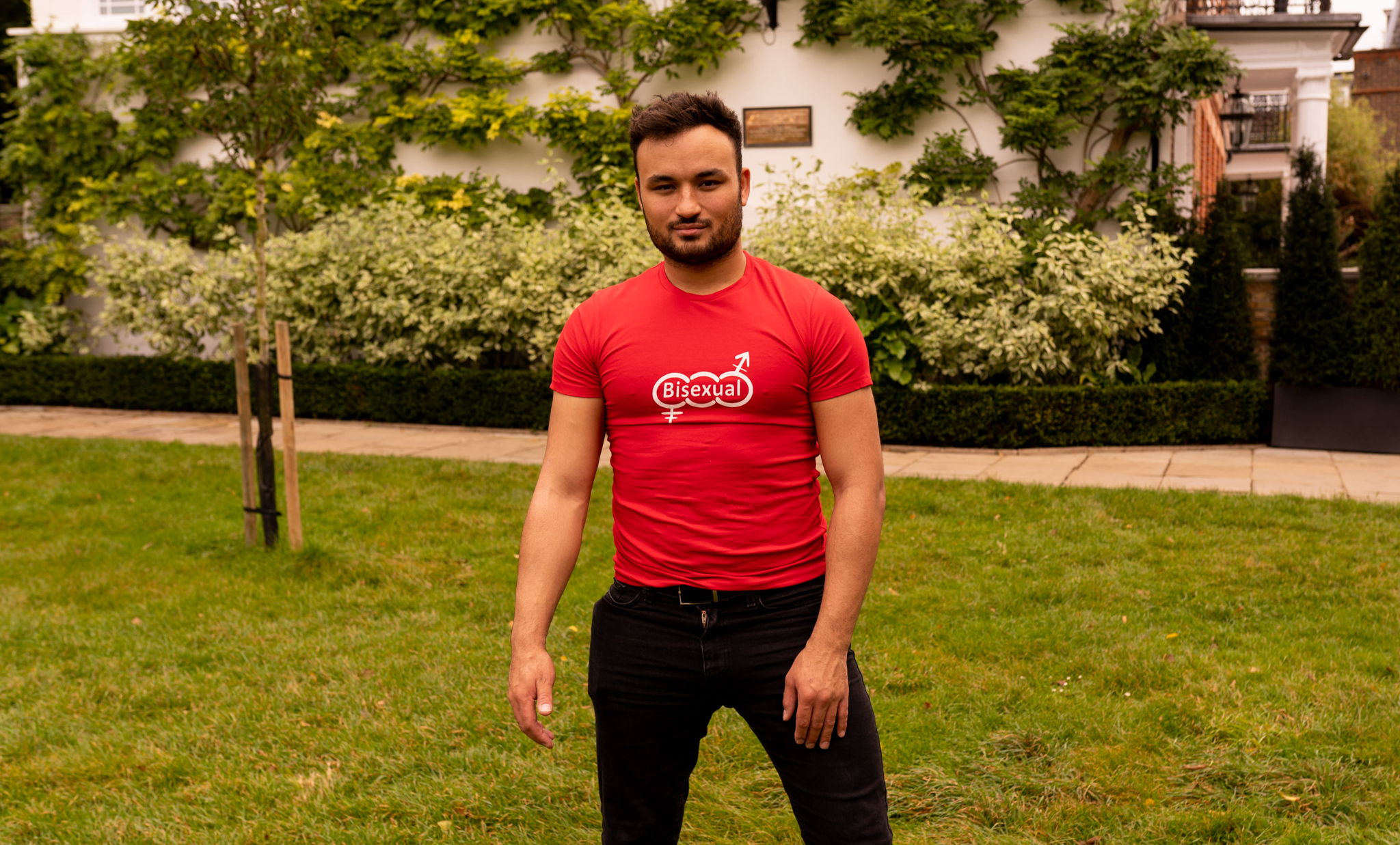 Lewis standing in a field wearing a shirt with the words bisexual on it. Smirking.