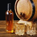 Petit fût de whisky en bois entouré d'une bouteille remplie de whisky et de deux verres vides