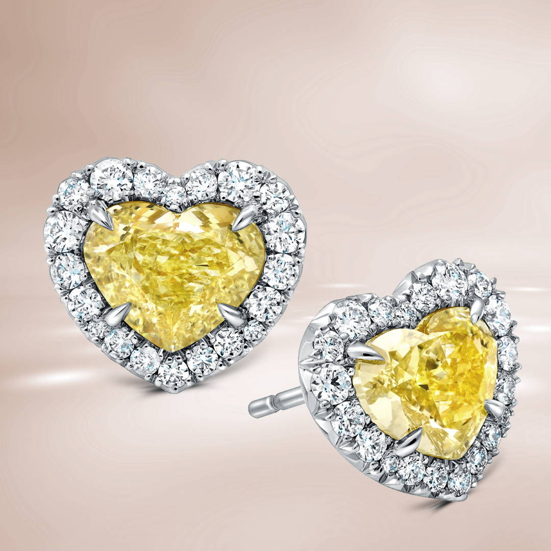 Heart shaped yellow diamond stud earrings with white diamond halos on a brown background