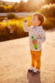 Toddler blowing bubbles while holding a bubble solution bottle, practicing breath control, and focused play in a natural setting.