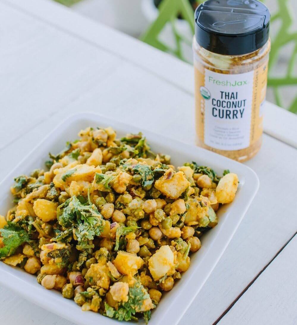 Bowl of coconut curry potato salad next to a large bottle of FreshJax Organic Thai Coconut Curry.