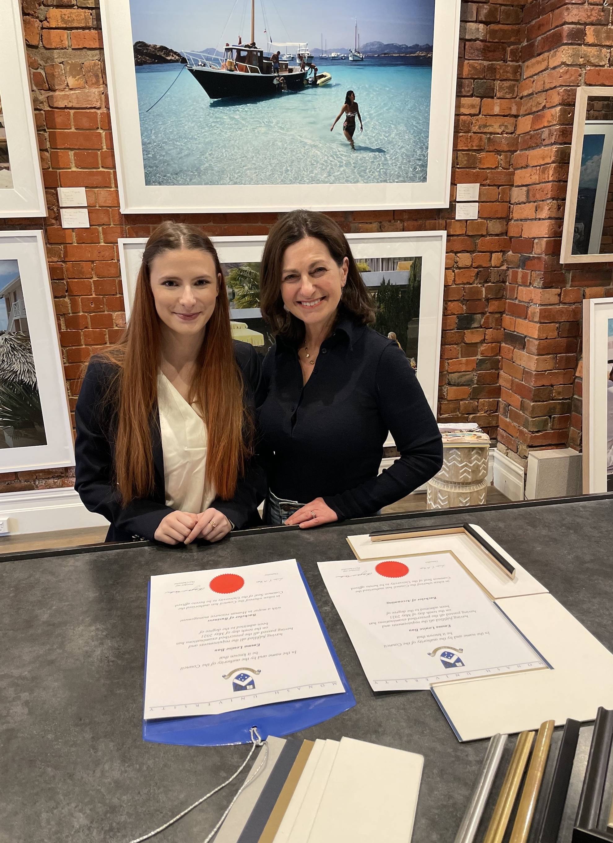 Cath and Emma standing at the counter with a selection of frame options and Emma's degrees, ready for framing