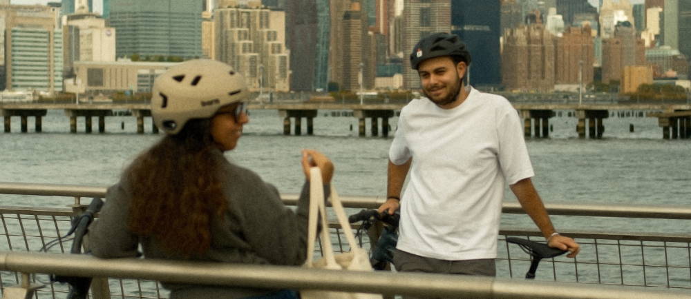 a man and woman in bike helmets talking near the water