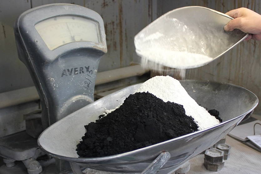 A person weighing powdered oxides on a scale, to produce Vitreous Enamel