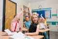 Children in classroom raising hands. 