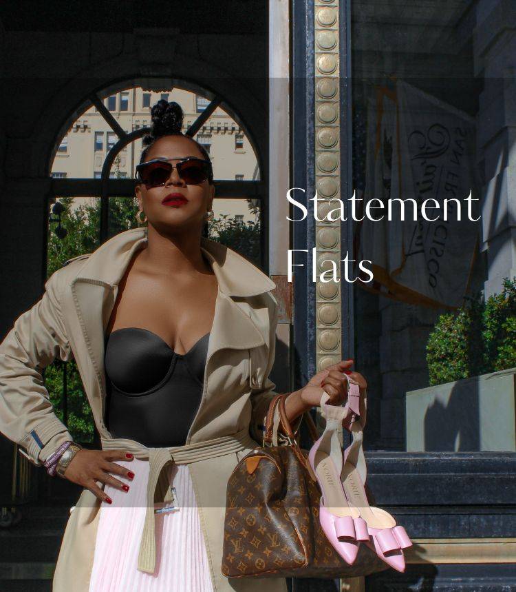 Black Woman looks directly at the camera holding pink closed-toe flat luxury sandals with bow on top