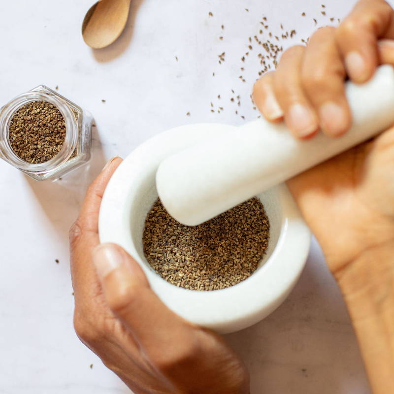 Ajwain seeds being crushed into a powder in a mortar and pestle