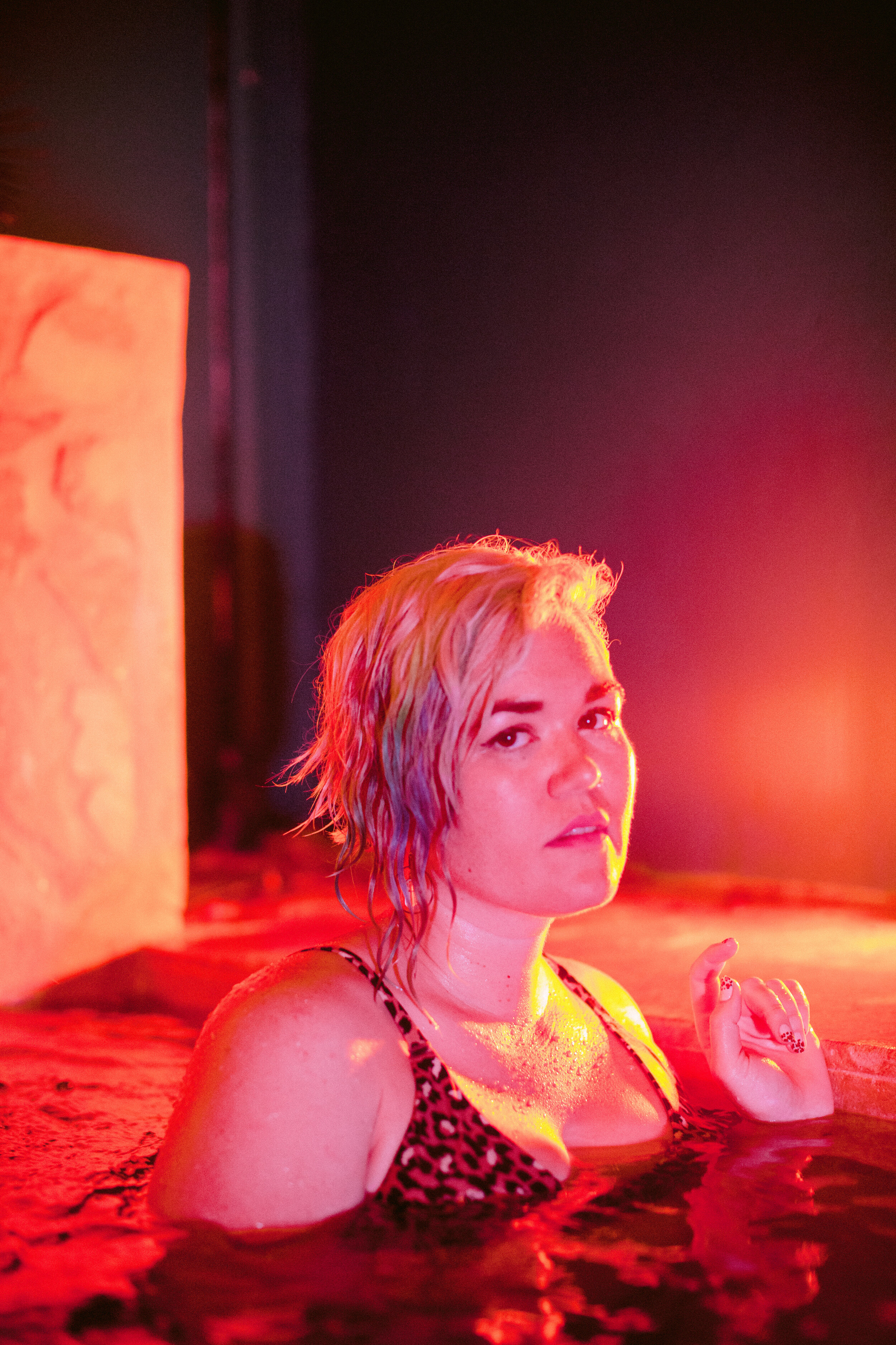 A woman with leopard pring swim top looks at the camera while in the water. Her hair is dyed rainbow.