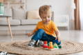 Cute boy in a yellow t-shirt sitting on a carpet and playing with multicolor wooden blocks. 