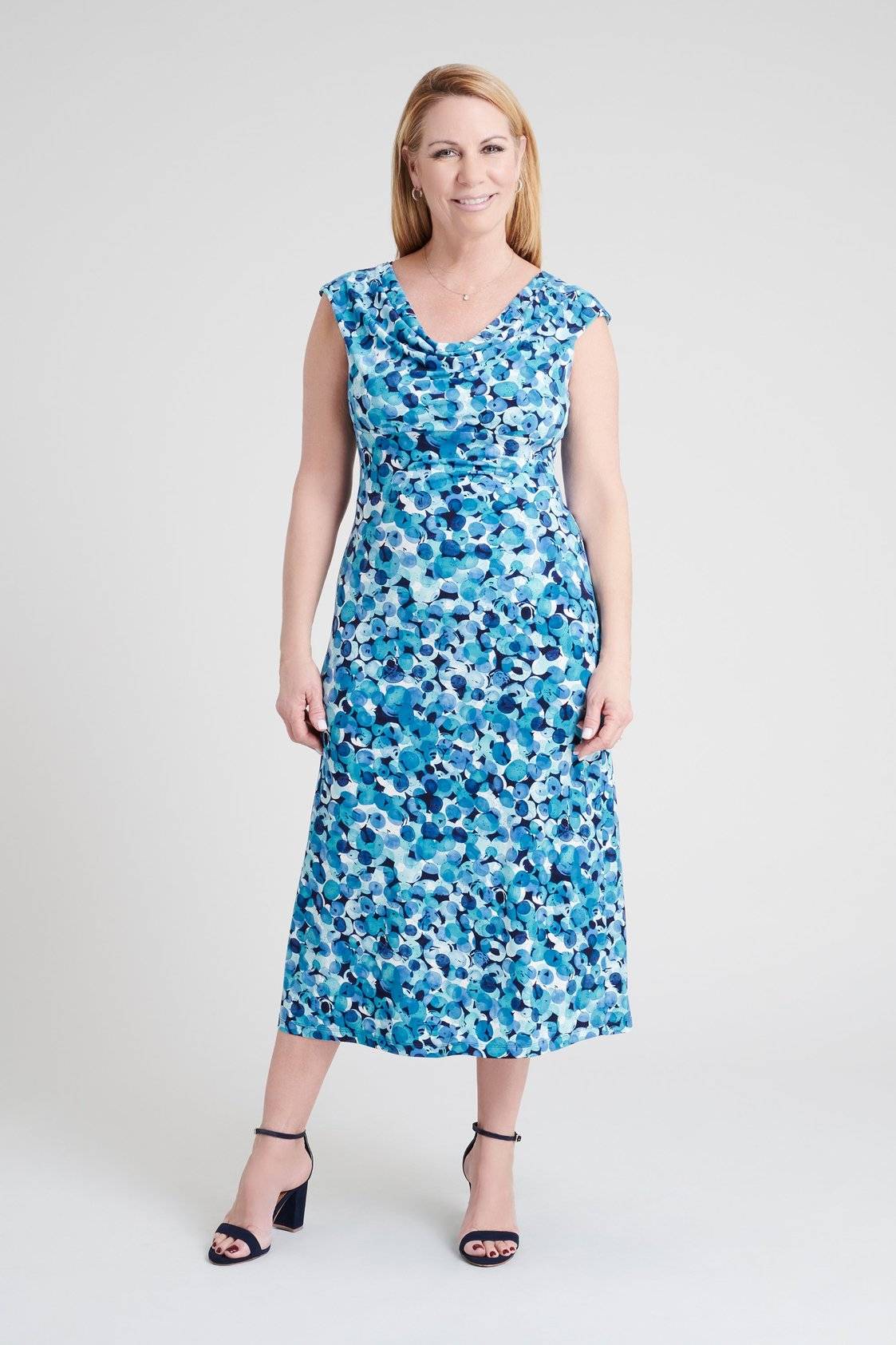 blonde woman posing in a studio wearing a multi-hue light blue bubble dot print calf-length sleeveless dress with cowl neck from connected apparel