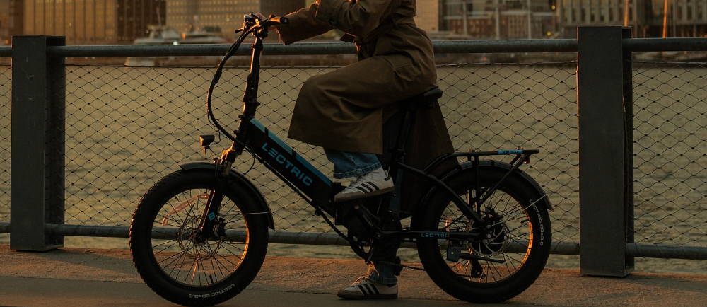 a woman standing over a lectric electric bike during sunset by the hundson river in new york city