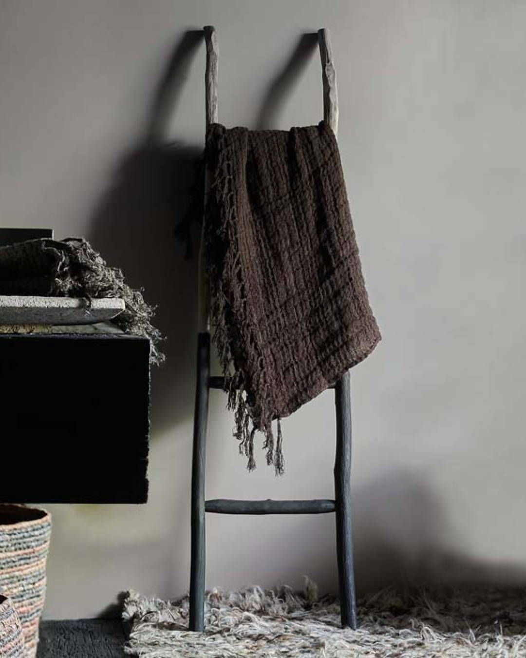 A decorative wooden ladder in a bathroom draped with a  brown linen throw