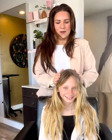 a hair stylist standing over a younger clent that is seated. The hair stylist is looking down at the clients dyed hair.