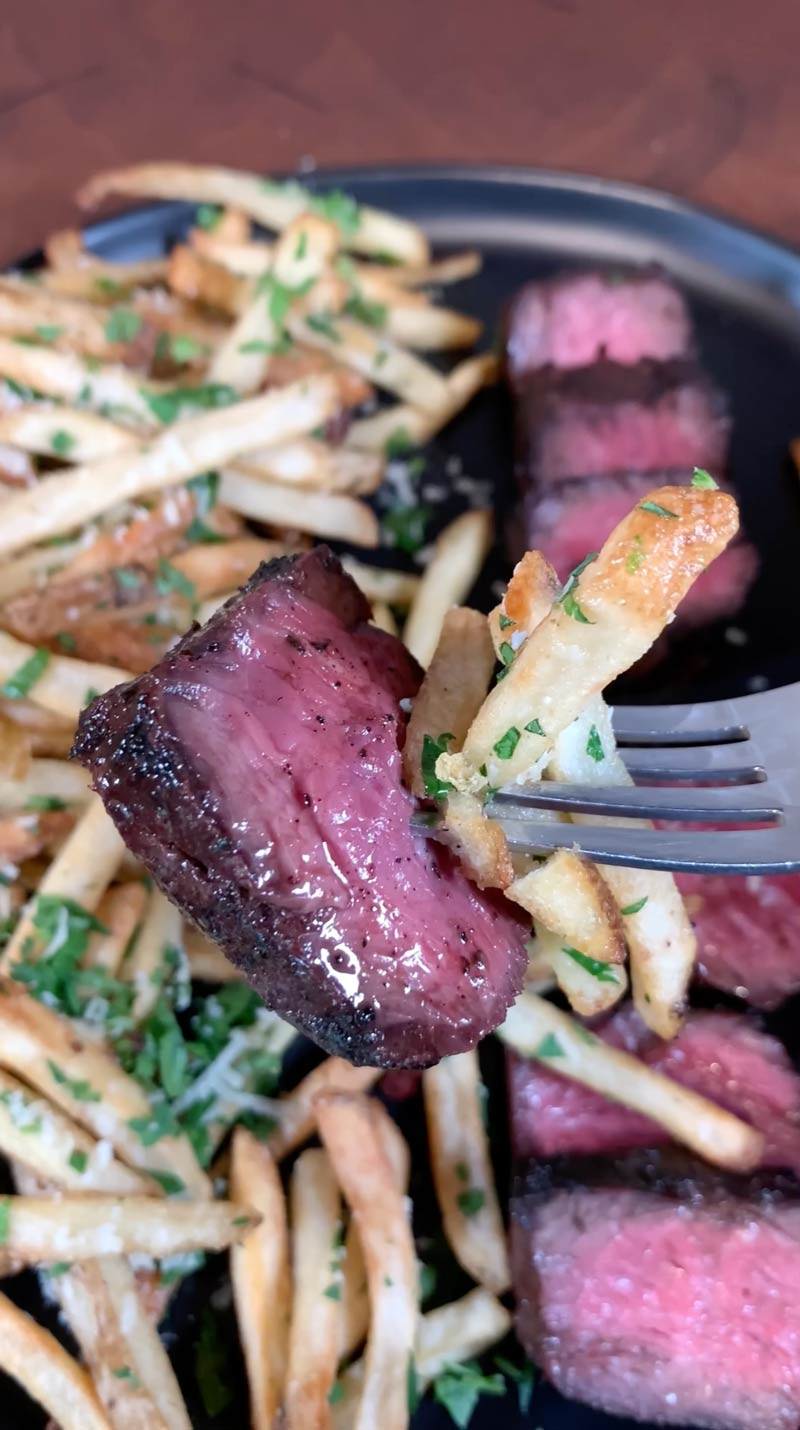 A medium rare slice of a Certified ONYA hanger steak from BetterFed Beef can be seen on a fork along with two french fries. 