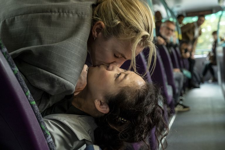 Villanelle and Eve laying on a bus seat kissing while the other passengers are looking at them.