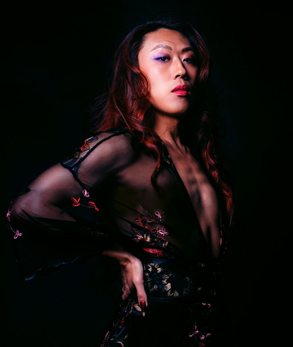 Nicky wearing a see through flowery dress and posing with her head held high against a dark background.