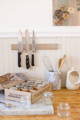 A brightly lit kitchen shows a cardboard box labeled 'Gneiss Spice' filled with glass jars sitting on a marble cutting board.