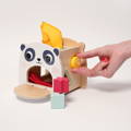 Hand placing a yellow shape block through a cutout on the Montessori Baby Tissue Box toy, with flap door opened and tissues visible inside.