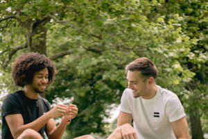 A pair of guy friends wearing shorts and shirts playing card games and laughing together.