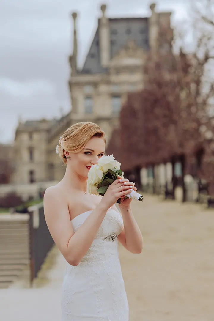 Photo de la mariée dans sa robe de mariée blanche. Elle tient des fleurs et sourit.